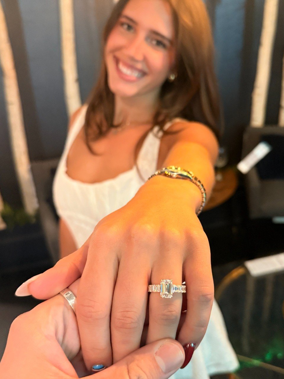 An emerald cut diamond ring with emerald cut side stones, worn on the hand of Axel's wife