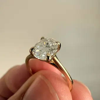 An oval solitaire in yellow gold held between two fingers